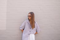 一位戴墨镜的时尚女性，在休闲的环境中倚着砖墙热情微笑