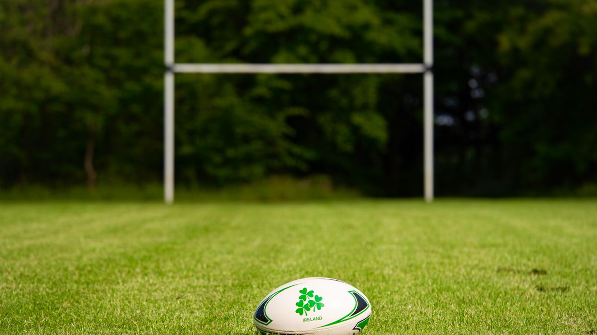 A rugby ball on a grass pitch in front of the goal posts