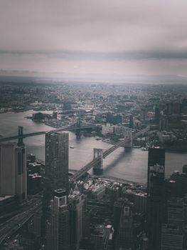 Aerial view of Brooklyn Bridge and Manhattan skyline in overcast weather, capturing urban landscape.