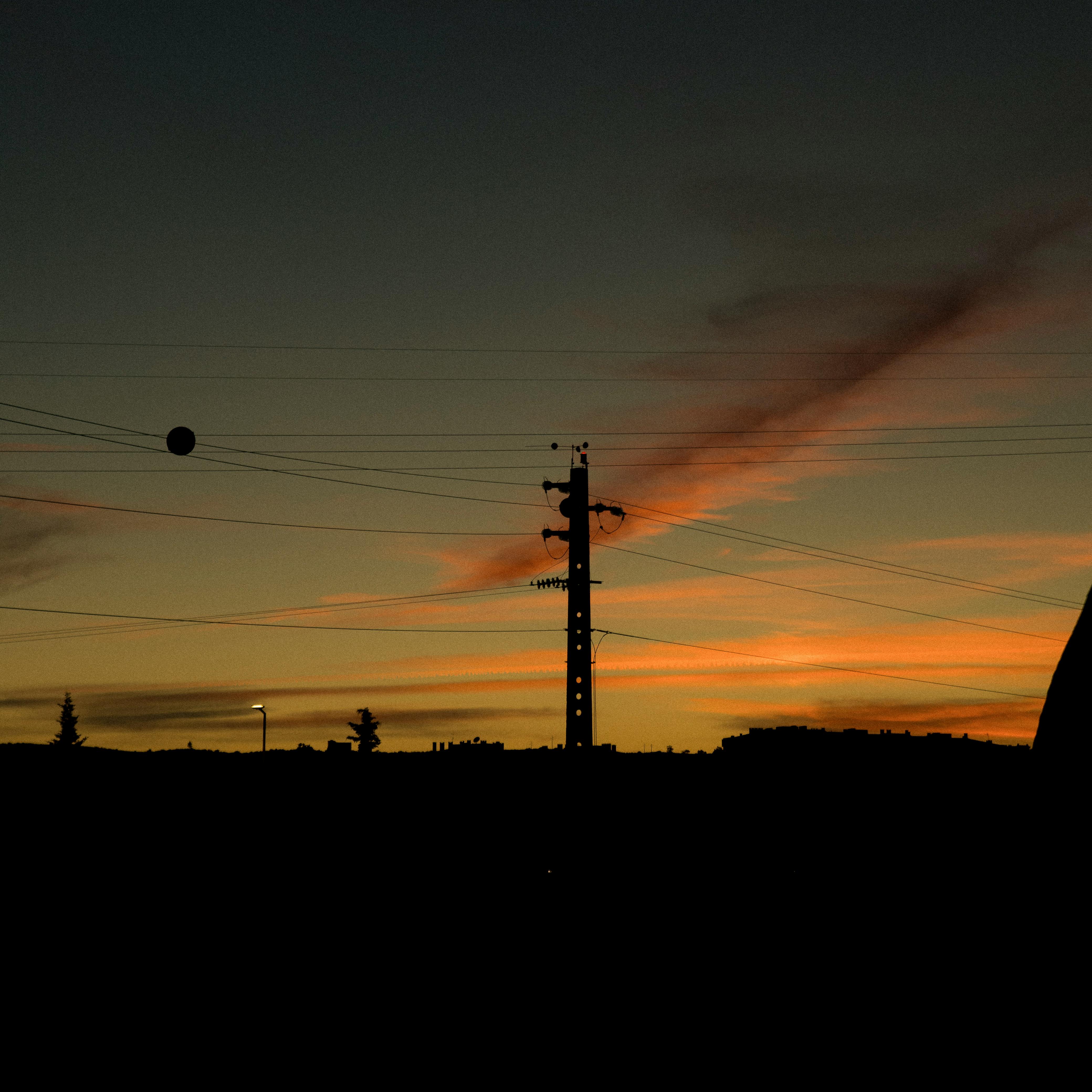 A silhouette of power lines and pole against a vivid, colorful sunset sky.