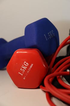A vibrant close-up of 1.5kg dumbbells and red resistance bands on a white background.