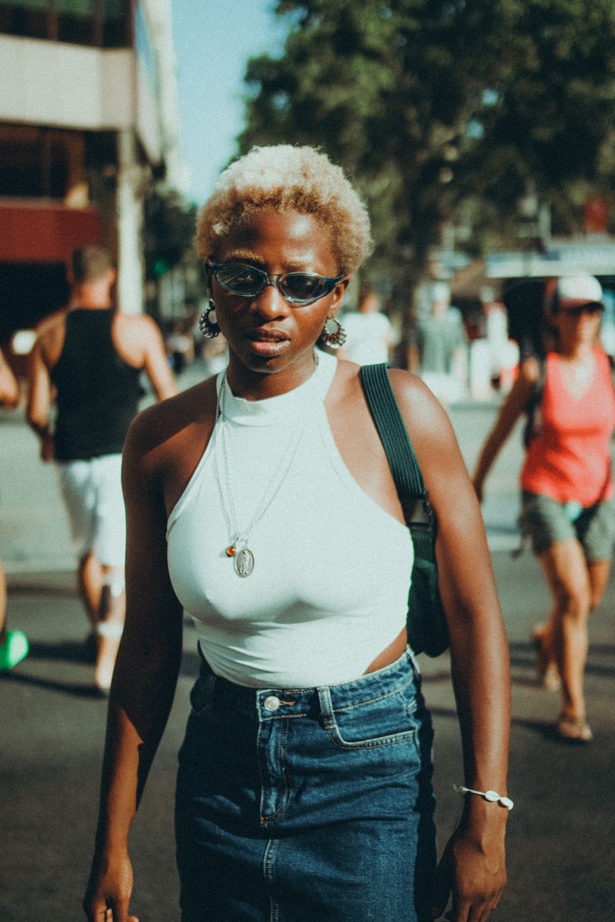 Woman in denim skirt and sunglasses captured in sunny urban street style.