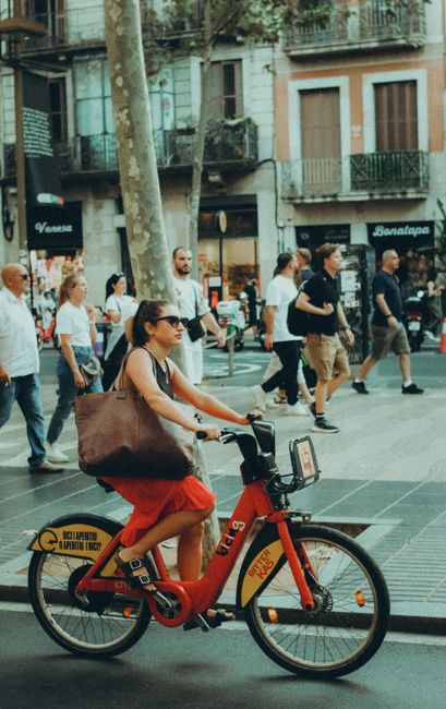Woman riding a shared bike on a city street with pedestrians in the background.