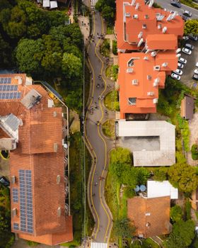 Aerial view of a winding urban street lined with red-roofed buildings and lush greenery.