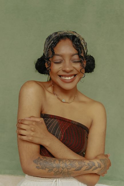 Smiling woman with a stylish tattoo and off-shoulder top, exuding warmth and style in São Paulo, Brazil.