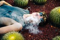 一名戴着墨镜的男子浑身是烟，躺在被仙人掌包围的红色砾石上