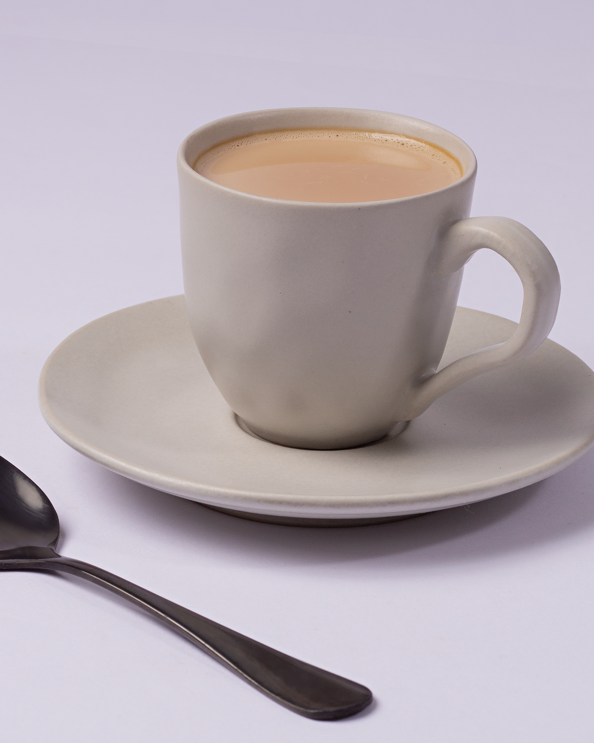 Elegant porcelain cup of coffee with saucer and teaspoon in a minimalistic setup.