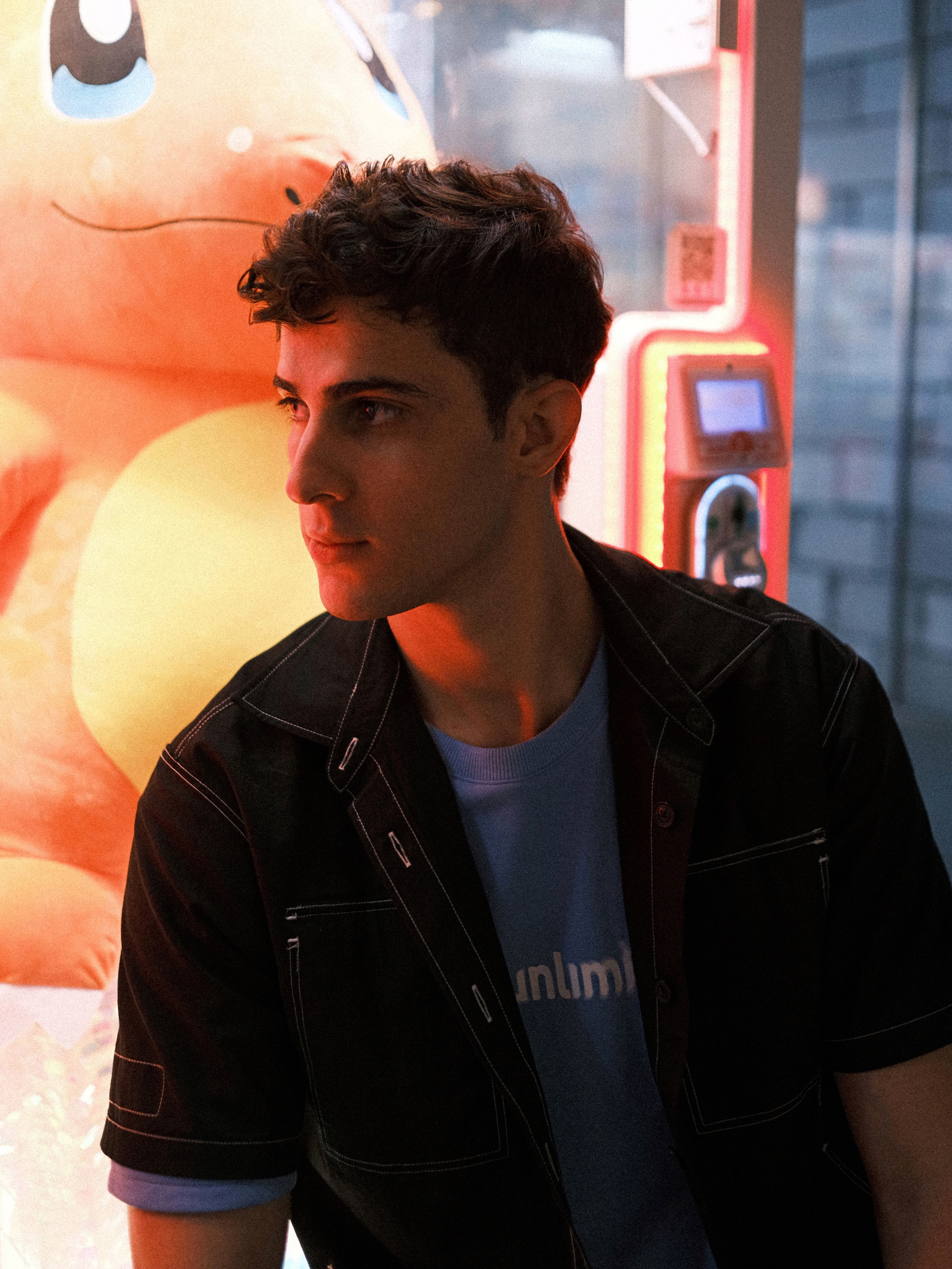 A young man in casual attire stands in front of an arcade machine, contemplating.