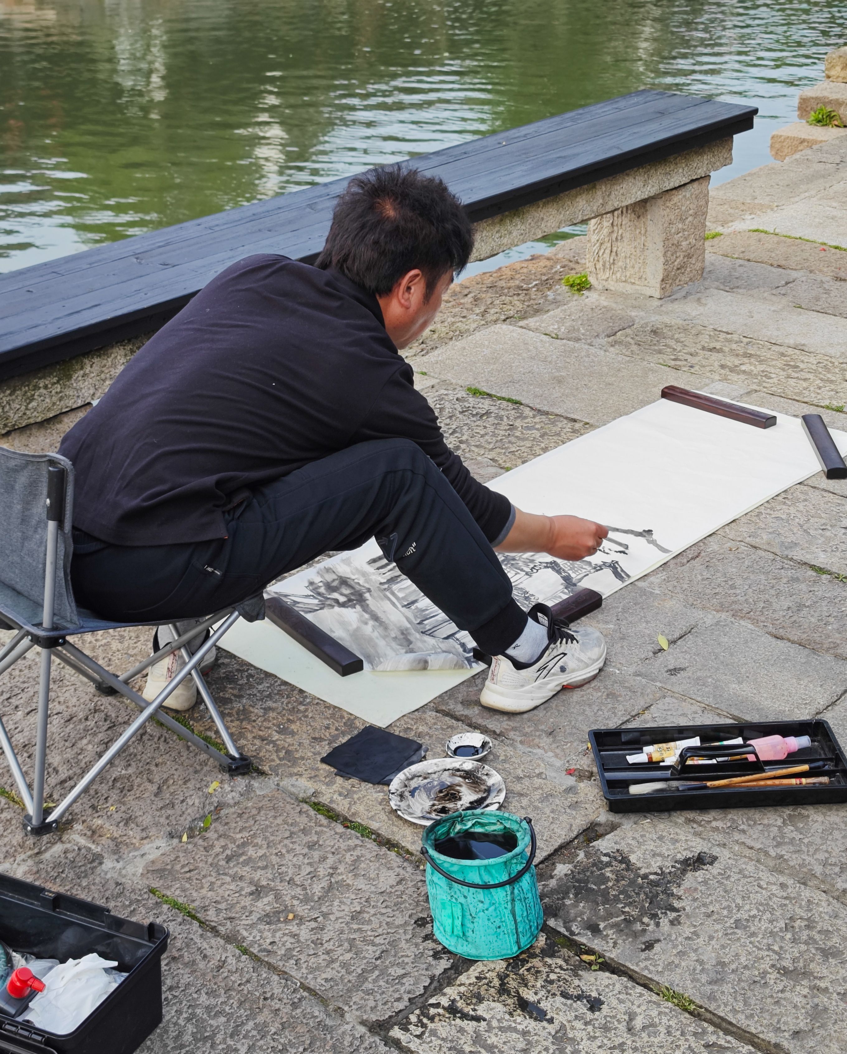 Artist engaged in painting by a river, showcasing creativity in Jiaxing's scenic setting.