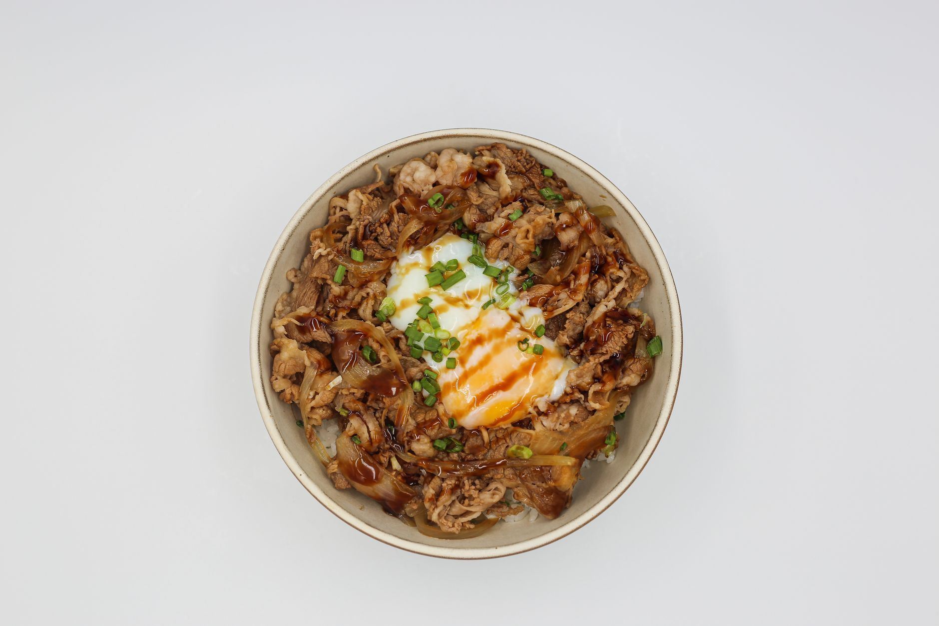 A flavorful beef rice bowl topped with a poached egg and green onions on a white background.