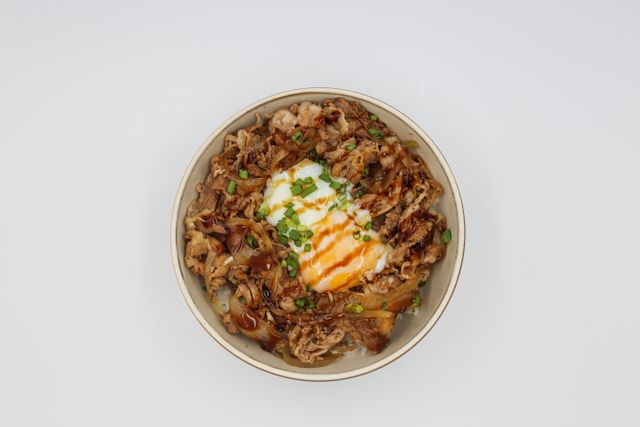 A flavorful beef rice bowl topped with a poached egg and green onions on a white background.