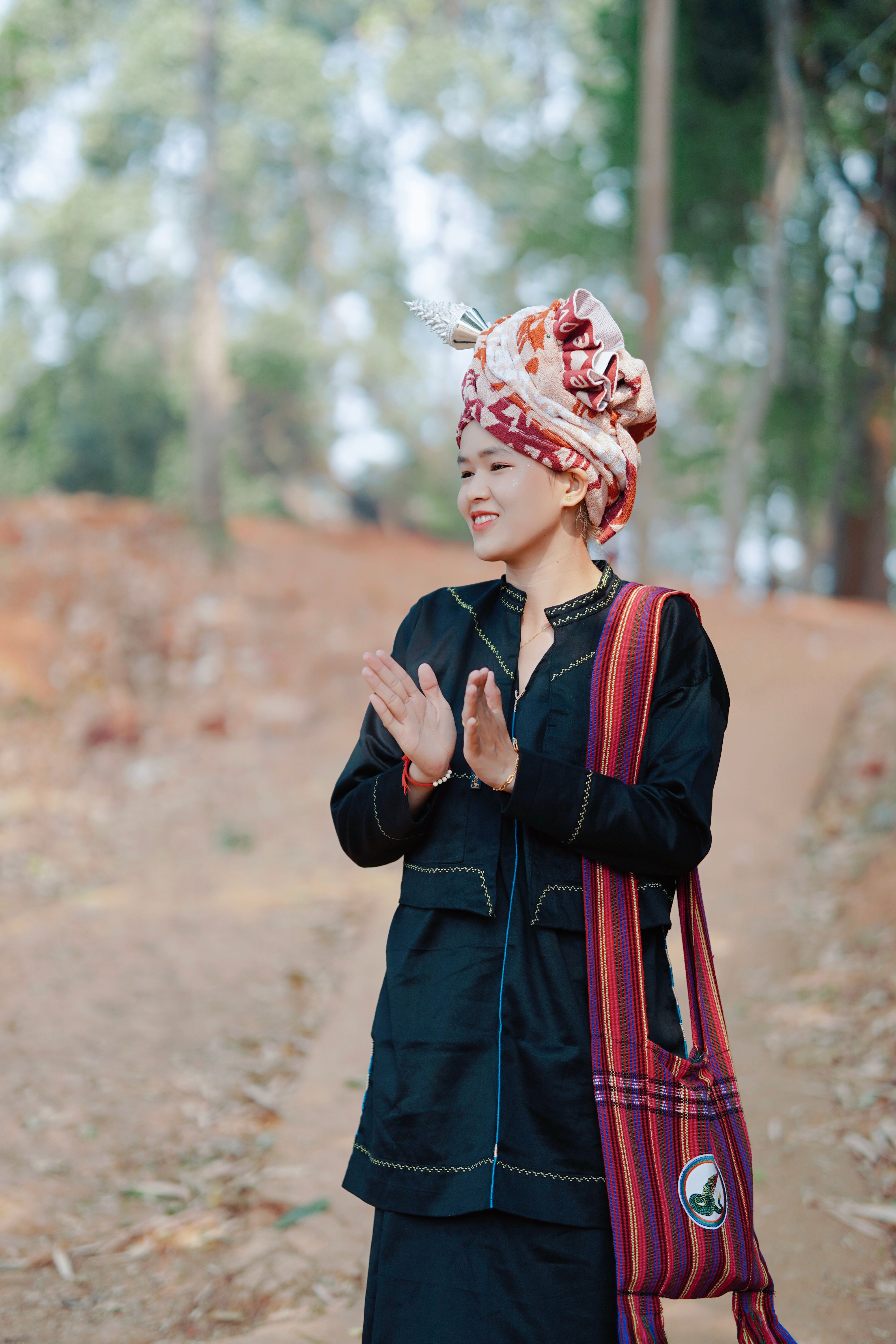 Asian woman wearing traditional clothing and hair wrap clapping hands outdoors.