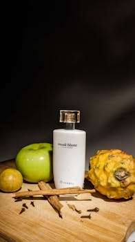 Still life of a perfume bottle with tropical fruits and spices on a wooden surface.