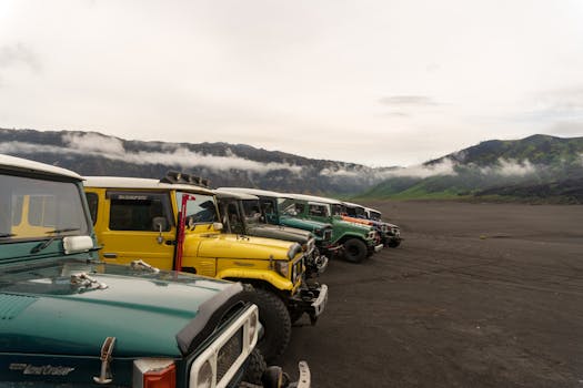 Classic offroad vehicles line up on volcanic terrain near mist-covered Mount Bromo.