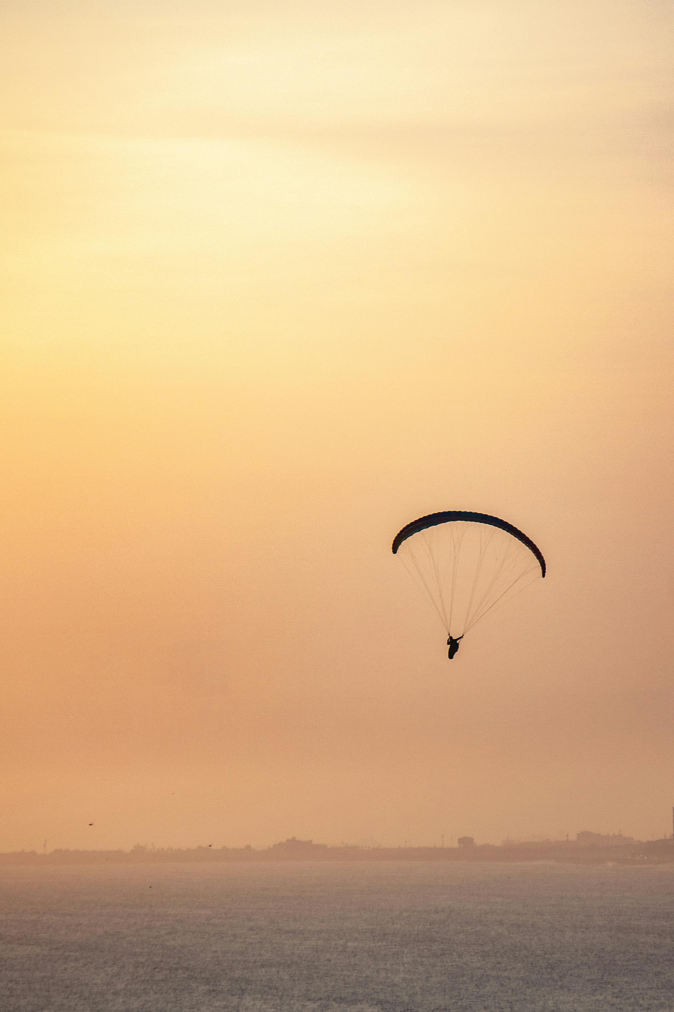 Dramatic silhouette of a paraglider flying over the ocean during a golden sunset.