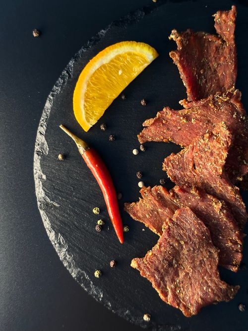 Free Close-up of a gourmet meat platter with dried peppers and an orange slice on a black slate. Stock Photo