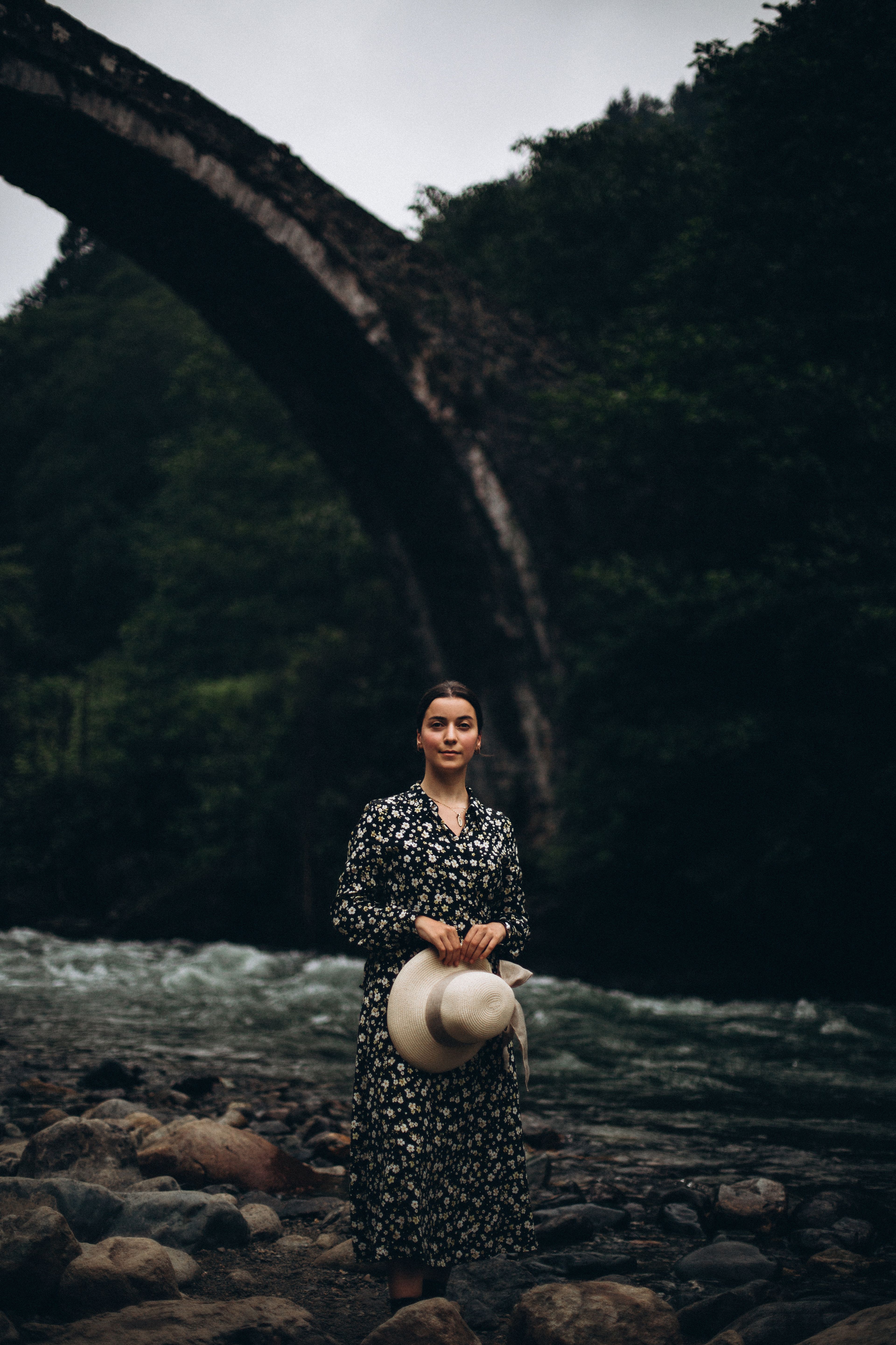 A Woman Standing on the Riverside near an Arch Bridge · Free Stock Photo
