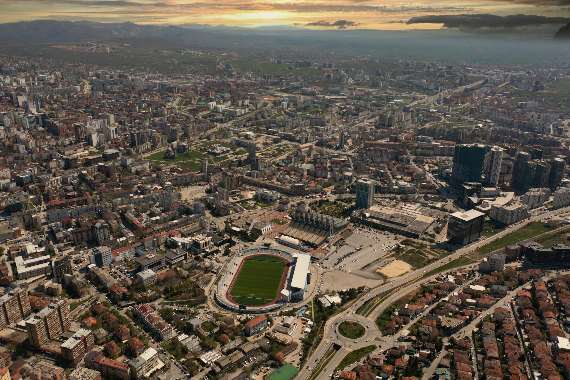 Dramatic aerial cityscape of Pristina, Kosovo featuring urban development and a prominent stadium.