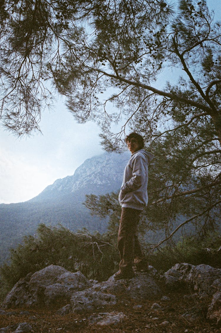 Young Man Standing On Rock In Mountains Landscape