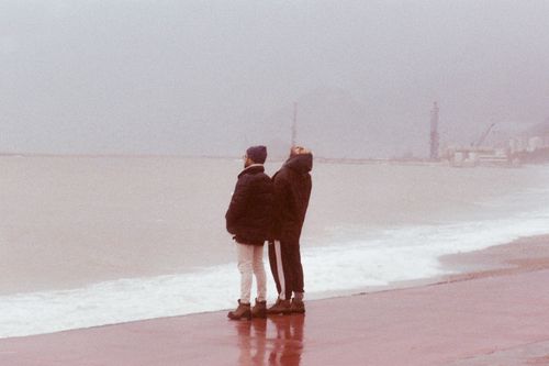 Free Two people in jackets standing by the sea on a foggy beach day. Stock Photo