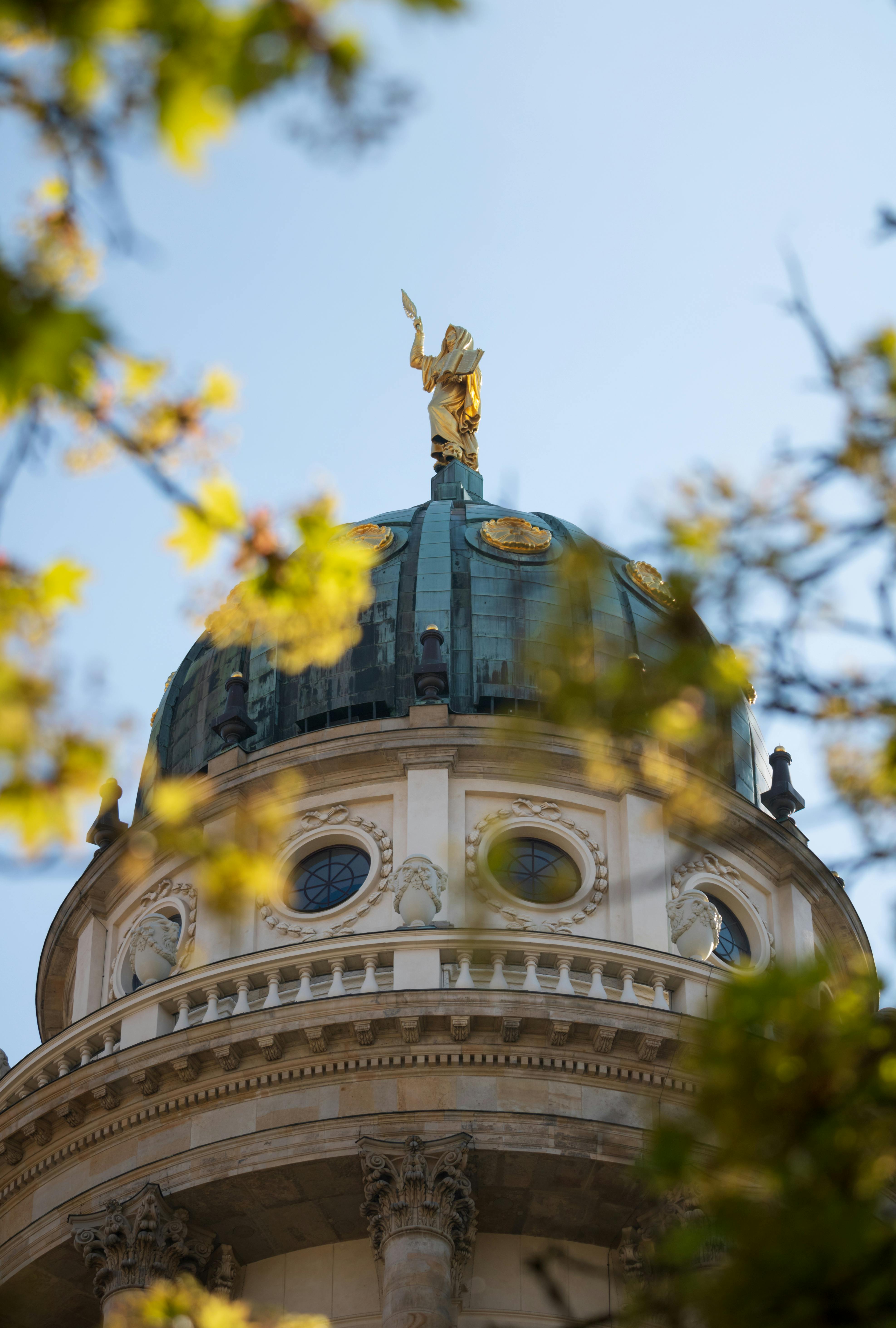Capture of the Französischer Dom in Berlin with golden statue amid spring foliage.