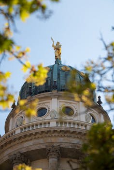 Capture of the Französischer Dom in Berlin with golden statue amid spring foliage.
