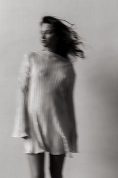 Black and white blurred portrait of a woman in a flowing outfit, capturing motion and emotion.