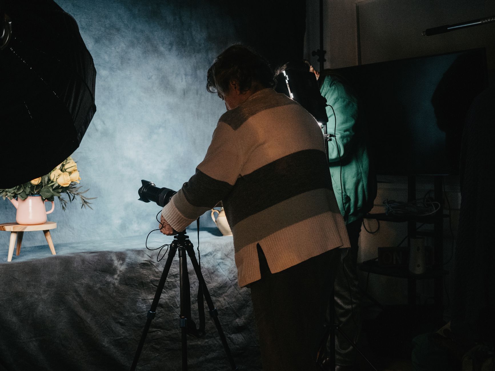 Photographer capturing still life setup with camera and tripod in professional studio environment.