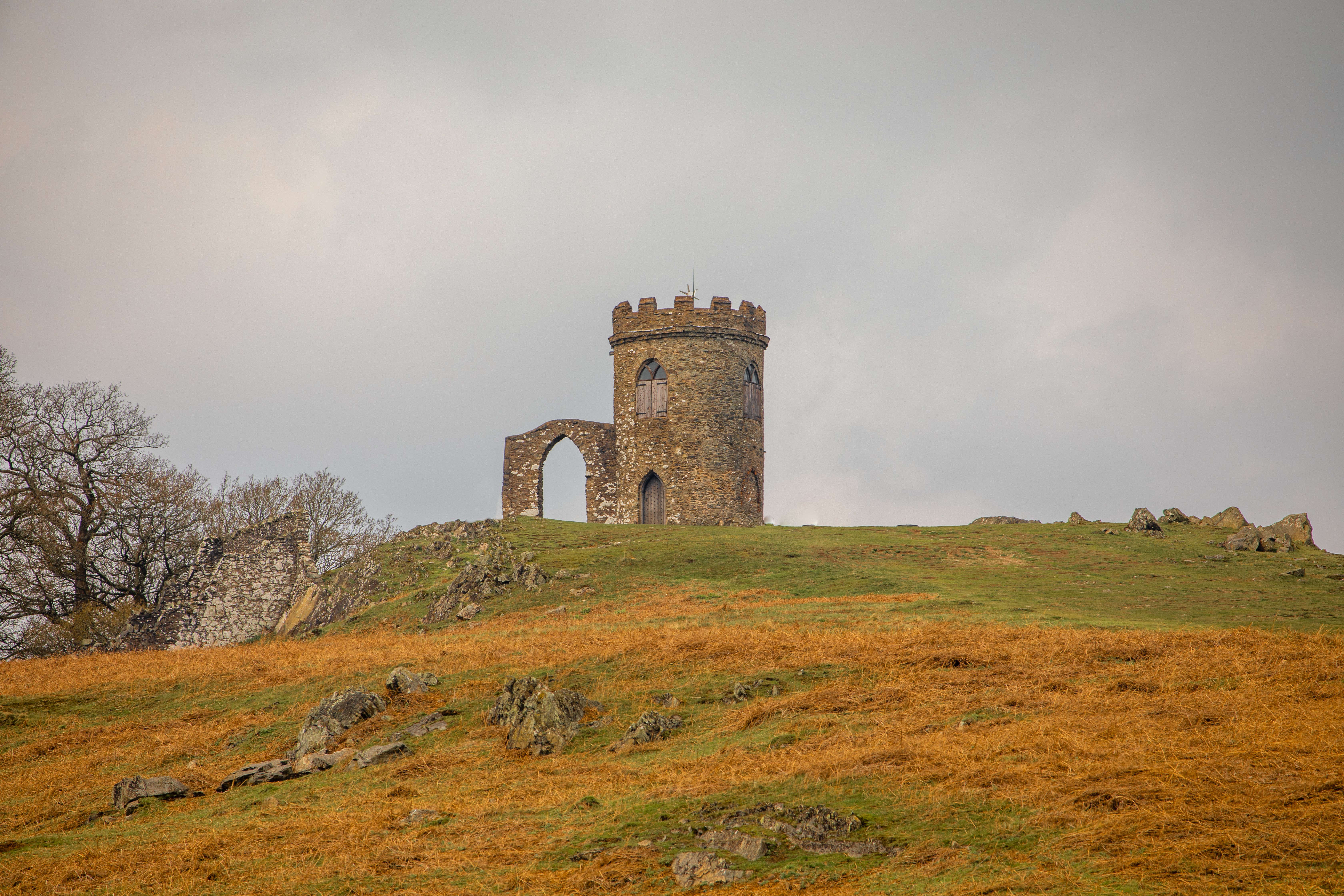 A scenic view of Old John Tower in Leicester, England, set against a grassy hill and cloudy sky.