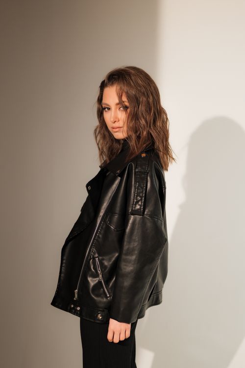 Free Fashionable woman with brown hair in a black leather jacket, standing against a white background. Stock Photo