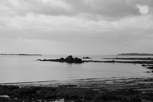 Free A tranquil black and white photo of rocks and sea under a cloudy sky. Stock Photo