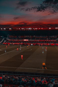 Wide-angle view of a soccer match taking place in a stadium at sunset with a vibrant sky.