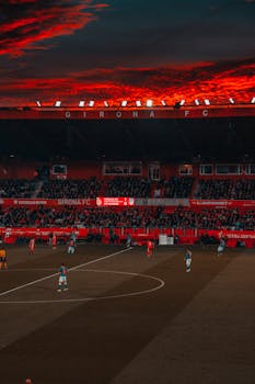 Dramatic evening soccer game at Girona FC stadium with vibrant red sky and intense play.
