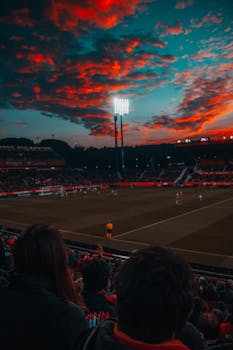 Dramatic sunset over a lively soccer game in a large stadium filled with spectators.