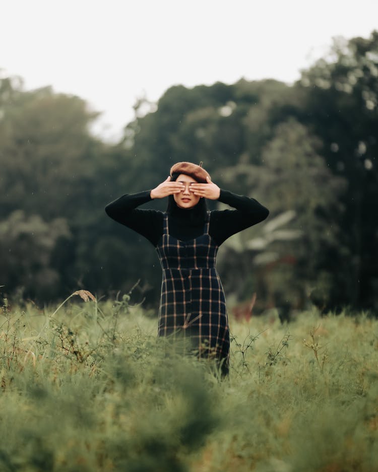 Girl Covering Eyes With Hands Standing In Field