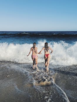 Two women in swimwear run into the waves at Bronte Beach, Australia, enjoying a sunny summer day.