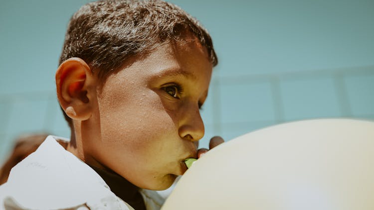 Sunlit Face Of Boy Inflating Balloon