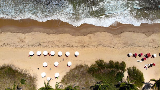 Stunning aerial view of a tropical beach with white umbrellas and crashing waves.