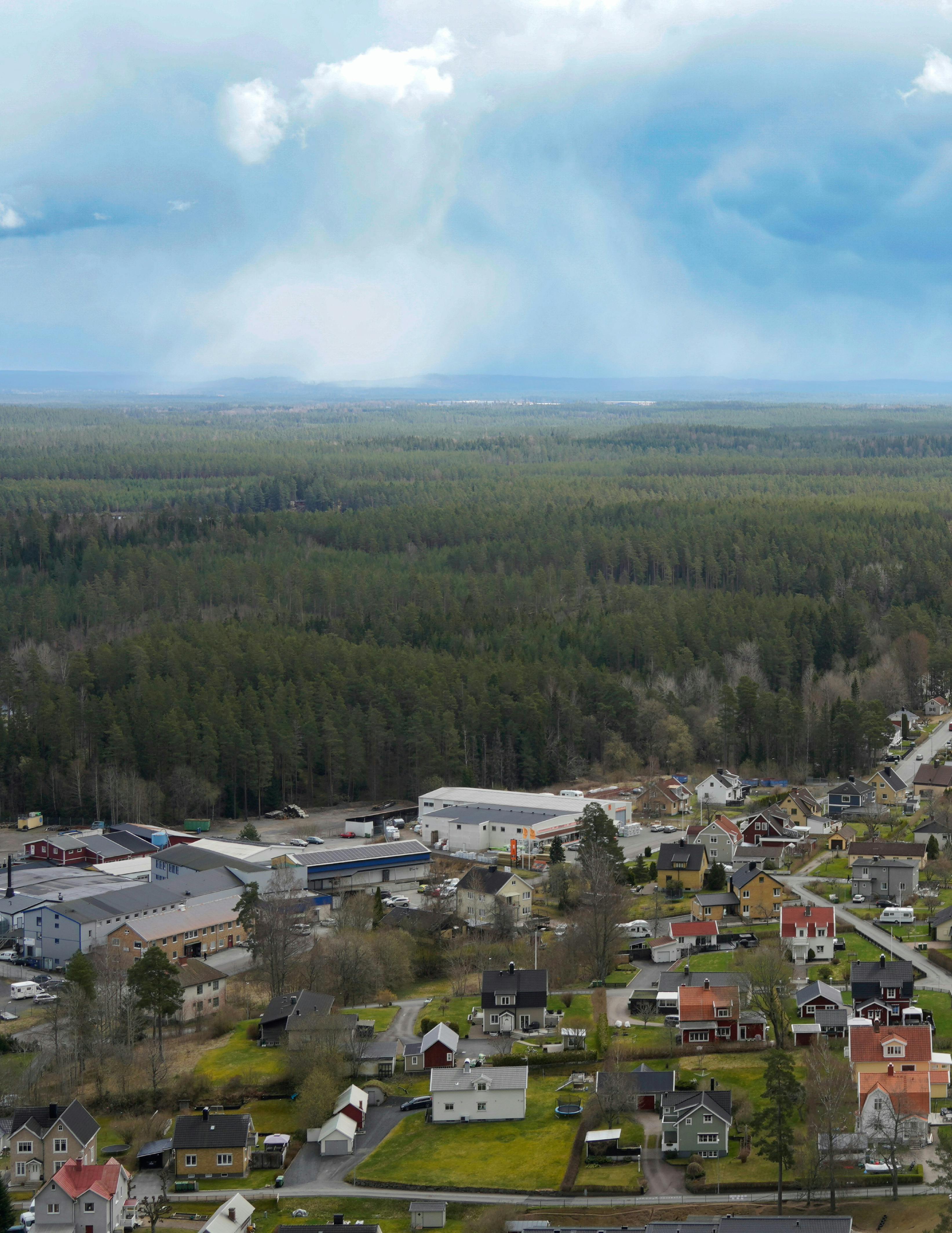 A scenic aerial view of a small town surrounded by a vast, lush forest and overcast skies.