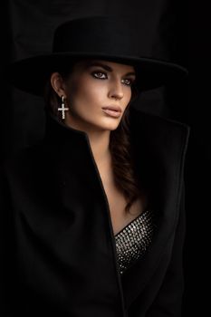 Stylish woman in black coat and hat exuding elegance in dramatic lighting.