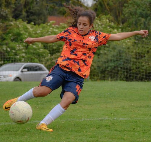 Free Dynamic action shot of a young female soccer player kicking the ball on a field. Stock Photo
