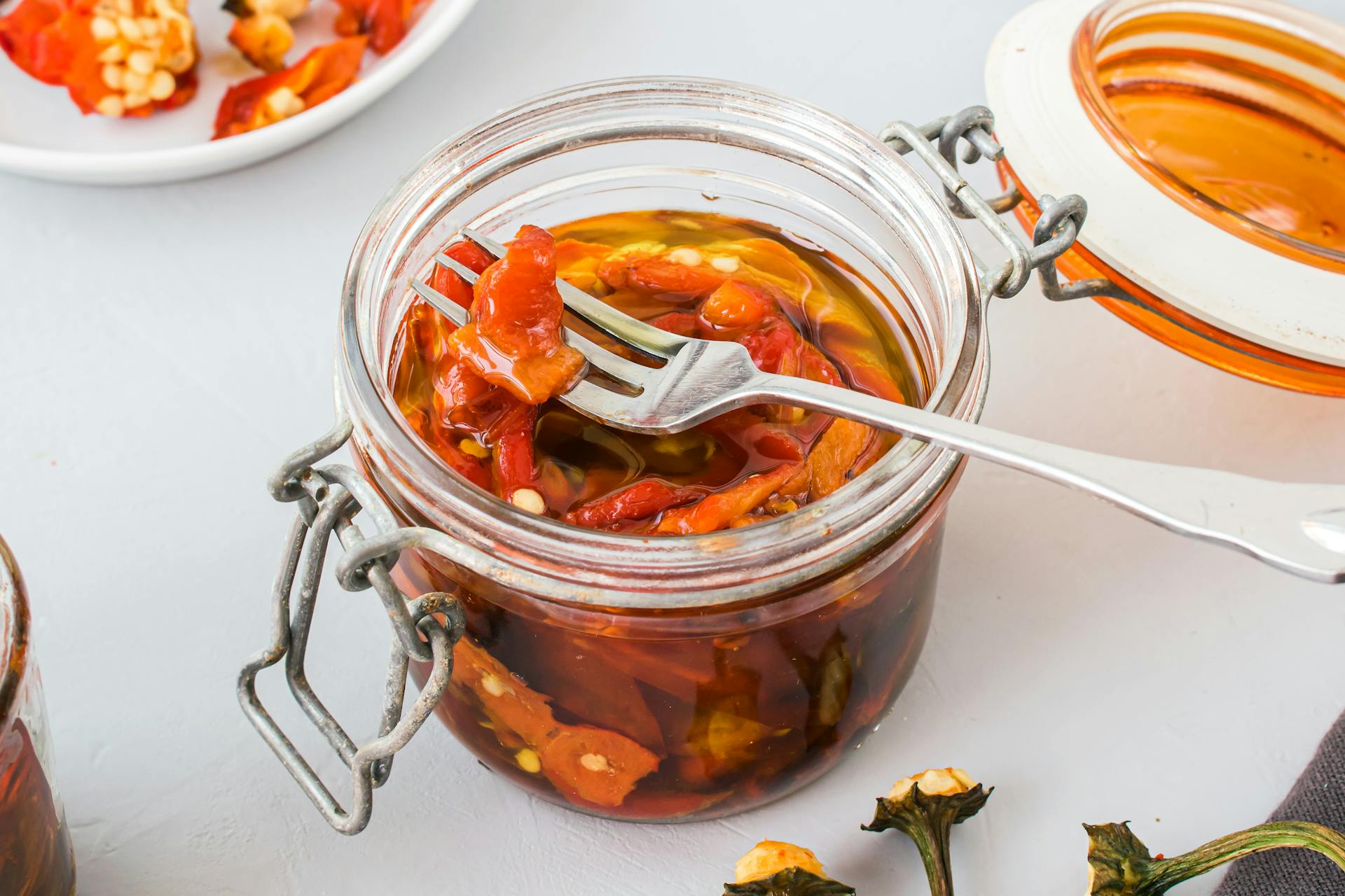 A jar of preserved red peppers in oil with a fork, perfect for food photography.