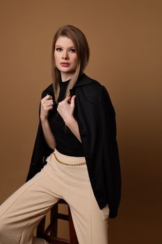 A stylish young woman poses elegantly in a studio, showcasing modern fashion and confidence.