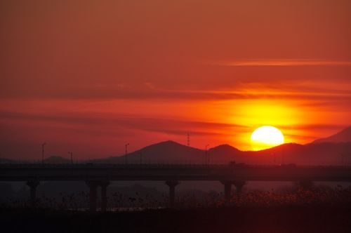 Free A stunning sunset over mountains and a silhouetted bridge captures nature's tranquility. Stock Photo