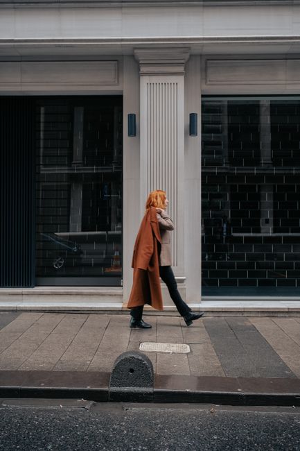 Stylish woman in fall attire walking past modern urban building on city street.