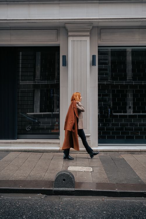 Free Stylish woman in fall attire walking past modern urban building on city street. Stock Photo