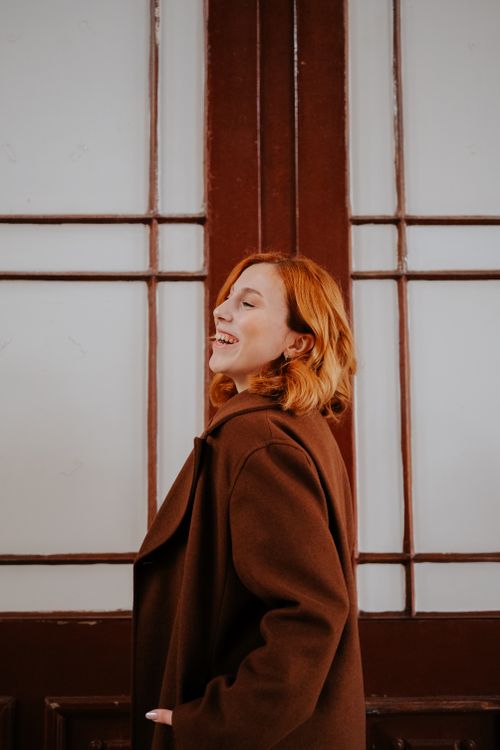 Free A woman with red hair smiles joyfully in front of wooden doors. Stock Photo