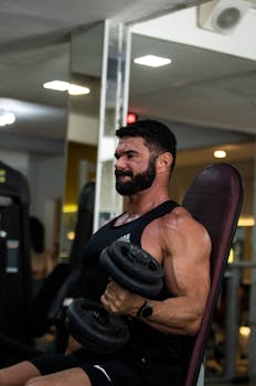 Muscular man with beard intensely lifting dumbbells during workout in gym.