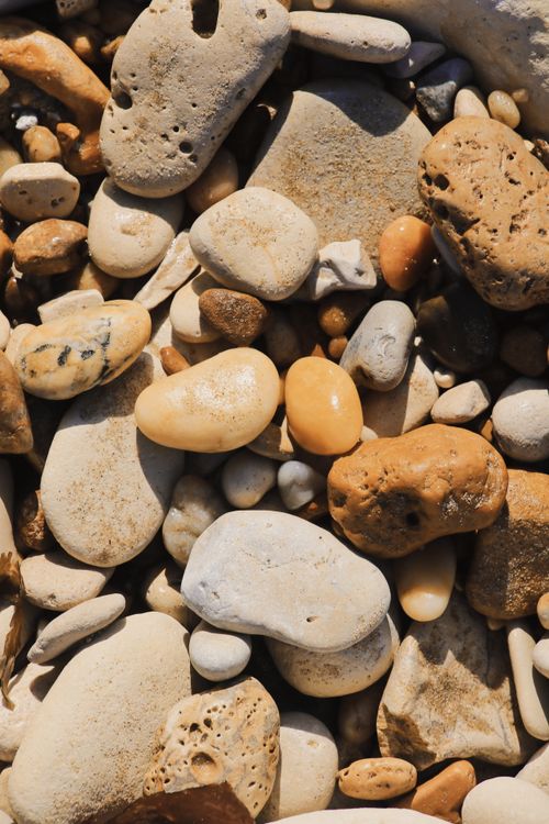 Free A close-up view of smooth, colorful pebbles and stones on the beach under bright daylight, showcasing natural textures. Stock Photo