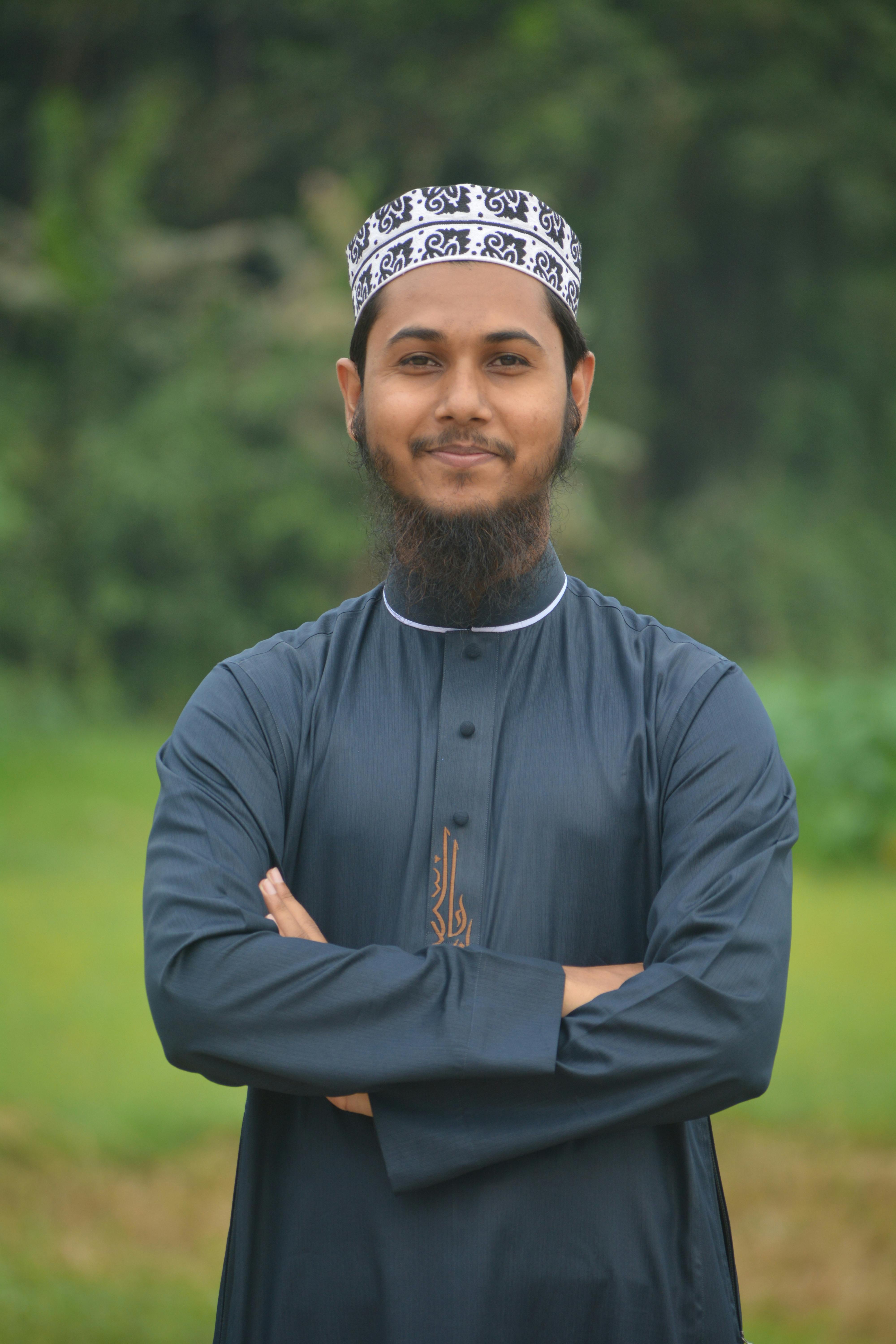Portrait of a confident man in traditional attire standing outdoors with arms crossed.